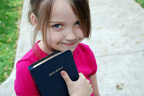 A little girl reading the holy bible A little girl holds on to her father's Bible outside church. praying child christianity family stock pictures, royalty-free photos & images