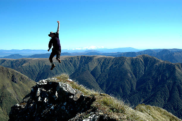 Hiker jumping for success atop a mountain stock photo