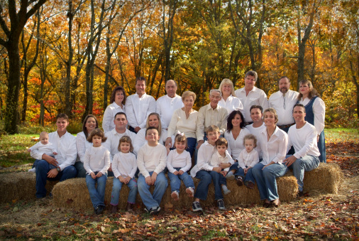 Outdoor portrait of a large family during a family reunion. Four generations are included in this photograph. Taken on location in the rural Mid West during the Autumn Season. Everyone is looking at the camera and has a pleasant expression.