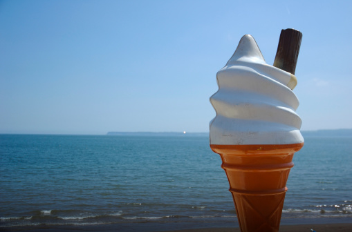 Giant ice cream cone stands without melting in front of a tranquil sea view