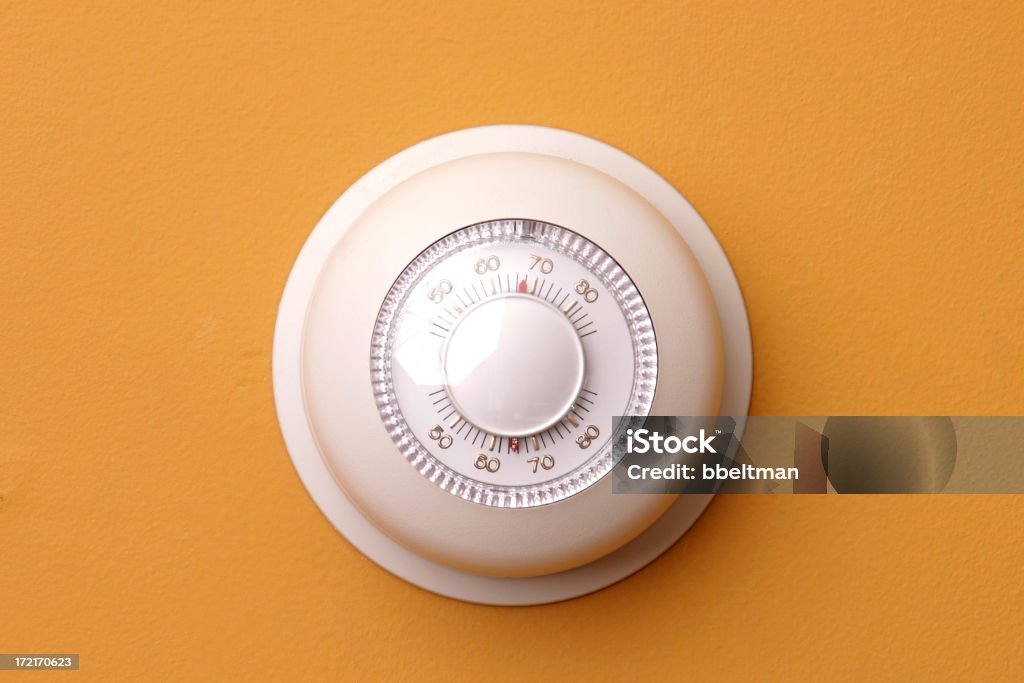 A closeup of a thermostat on a orange wall set to 68 degrees round thermostat on orange wall Thermostat Stock Photo