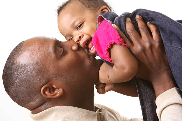 An African American father holding and kissing his daughter stock photo