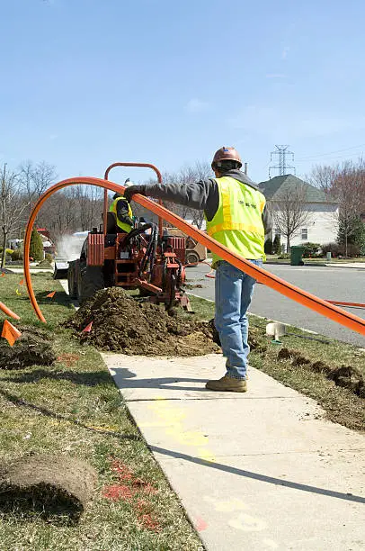Two installers work together to install conduit for fiber optic cable.