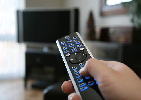 female hand hold tv remote control and press button to turn on television, sitting on couch in living room at cozy apartment, entertainment and relax at home