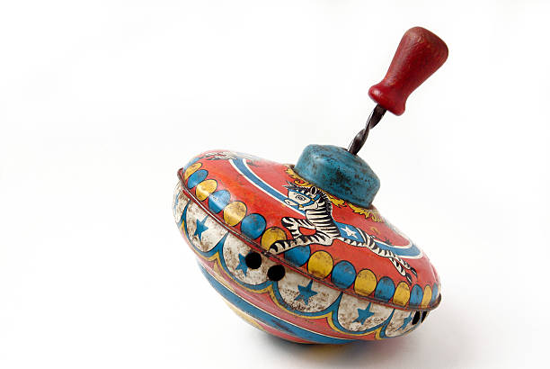 Antique Brightly Painted Metal Child's Toy Spinning Top Studio image of a very old metal spinning top photographed on a white background. The top is brightly painted with a merry go round theme. The paint is very worn and the top has some dents. spinning top stock pictures, royalty-free photos & images
