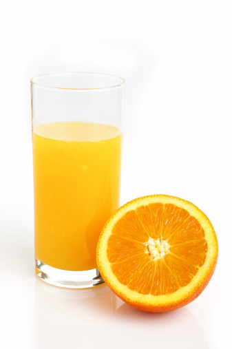 Fresh orange juice and orange fruit are in a basket on a white wooden background.