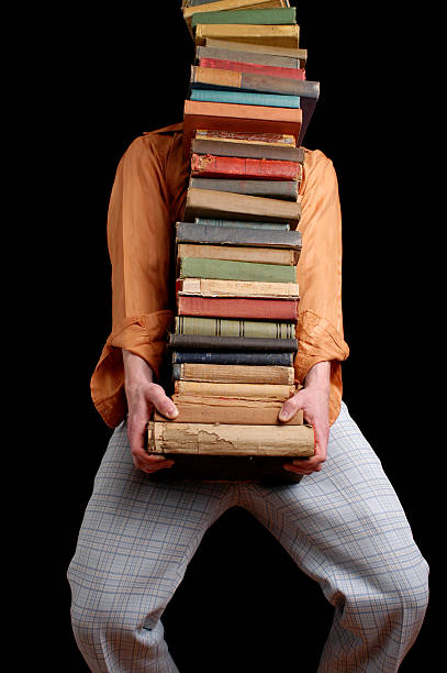 Man in retro clothing straining to carry a huge stack of vintage books.