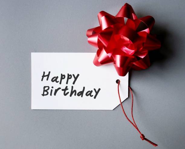 istock Red gift bow and white gift tag with hand written text HAPPY BIRTHDAY , on gray background, concept of simple birthday wishes 1721718610