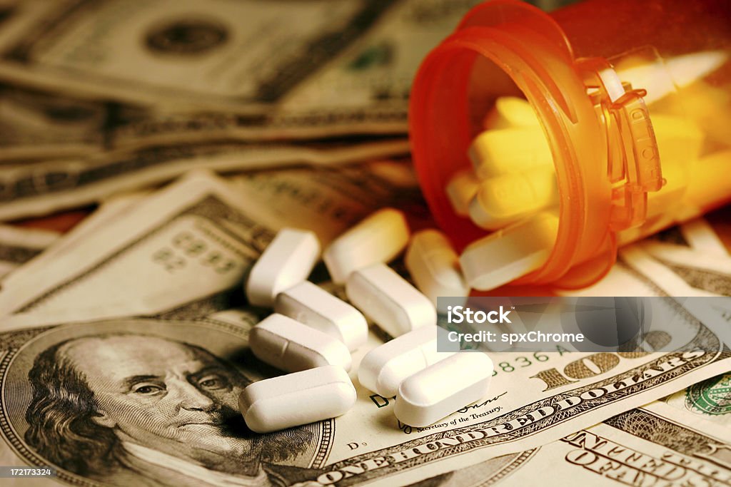 High Cost of Healthcare "Open bottle of pills on top of money, focus on bottom pills.  The rising cost of healthcare." Currency Stock Photo