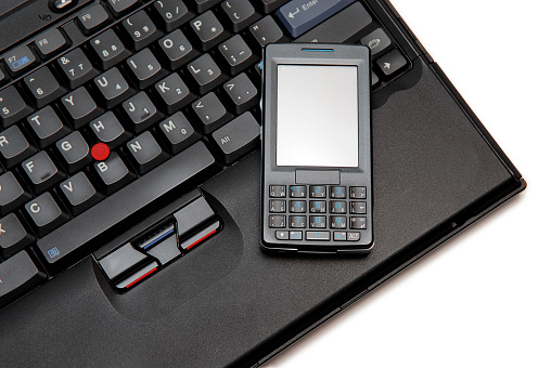 A modern, black smart phone on a laptop.