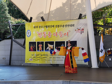 Seoul, South Korea - October 25, 2022: Korean traditional female young performer on the stage at Marronnier Park. There are two audiences sit to watch the musical dance performance.