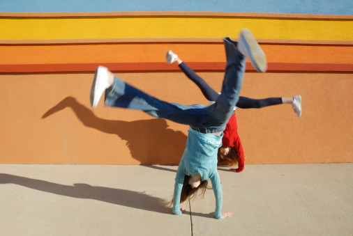 Adolescent twins doing simultaneous cartwheels outside a colorful building. Light and shawdows. Blurred motion.