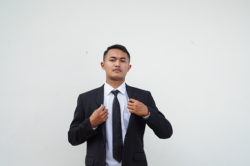 Handsome young businessman straightening his black suit on white background