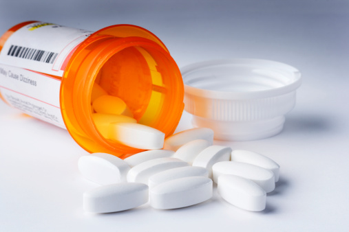 Prescription pills for healthcare and medicine, with group of white capsules spilling onto table from an opened, labeled bottle lying on its side. Close-up still life of pharmacy orange container package with lid off and medication poured, for concepts of health safety, dosage, overdose danger, illness, relief, and pain management. 