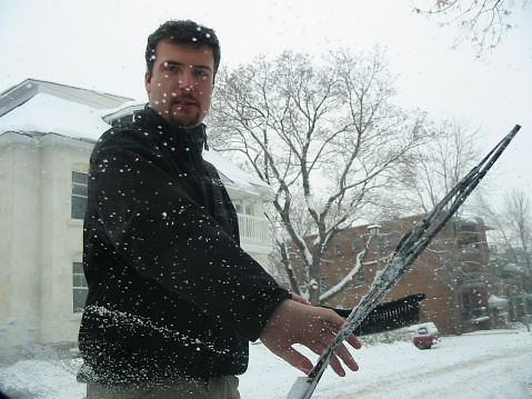Man cleans a windshield on a snowy morning.