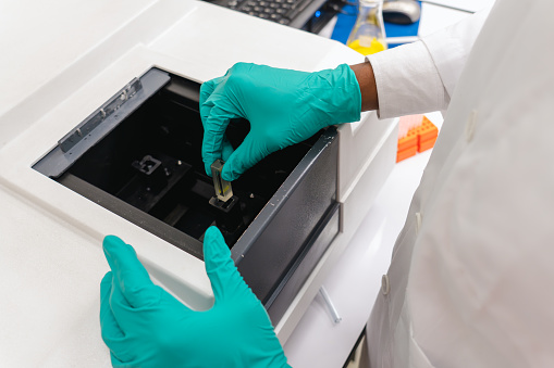 Scientist putting liquid sample container into specimen holder of laboratory spectroscopy for analyzing sample characteristics, scientist setting up experiment for research and education in university