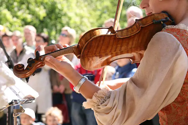 Girl in old-fashioned clothes playing on fiddle. Focus on foreground. Blured music-desk and people in the background.Similar photos: