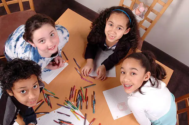 A happy and diverse group of children draws at a table. Also available: