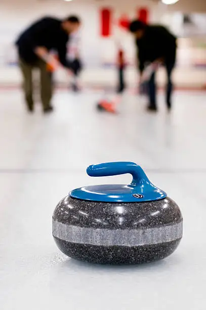 Curling rock with teammates sweeping in the background.