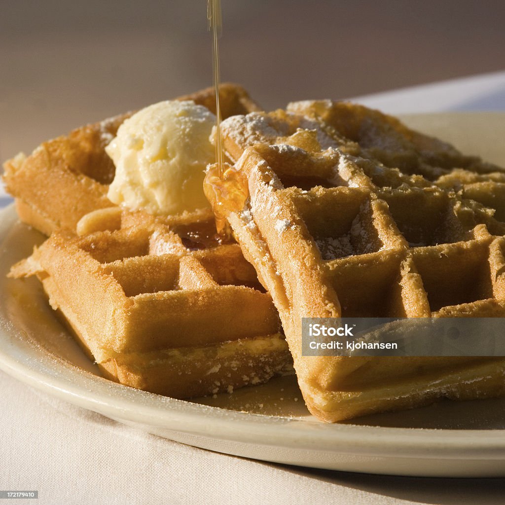 Belgian Waffles with Butter and Syrup Syrup being poured onto freshly-made Belgian waffles at a cafe early in the morning. Waffle Stock Photo