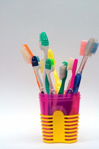 A pink and yellow cup filled with toothbrushes.