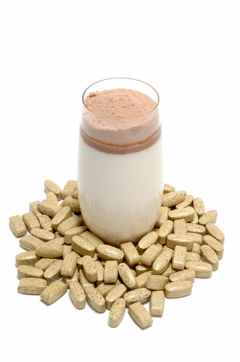 Glass of milk with portion whey protein, surrounded with tablets of fat burner.