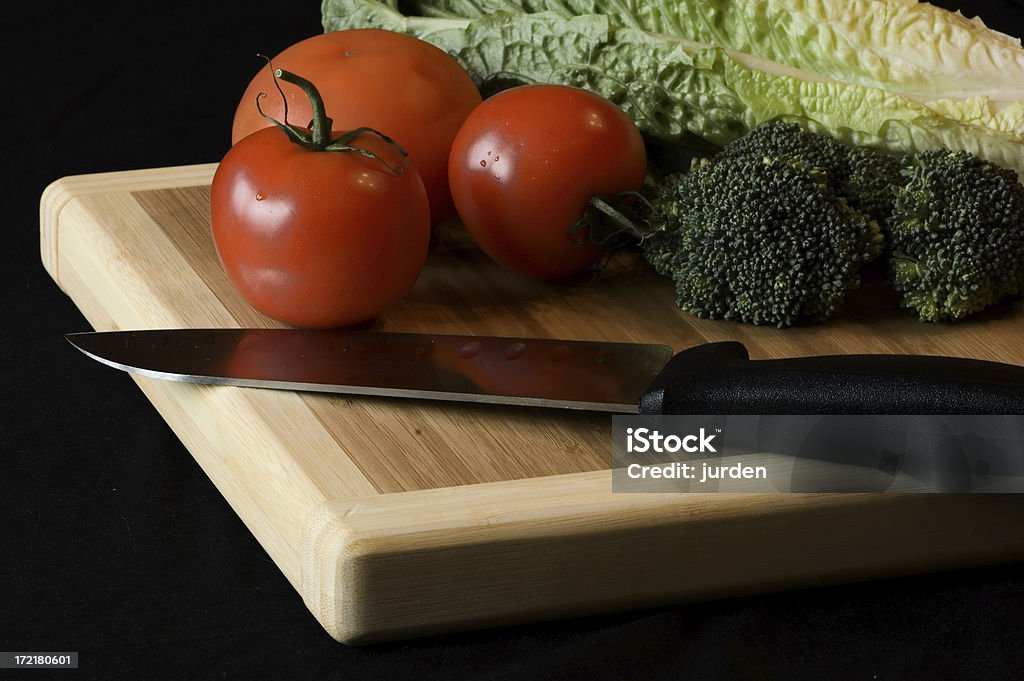 Tomato, broccoli and lettuce "Tomato, broccoli and lettuce on a cutting board with a black knife.  On black background." Black Background Stock Photo