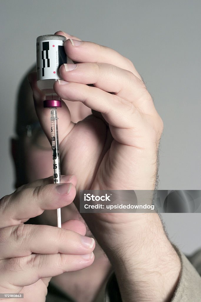 Filling a Syringe "Man (could be a doctor or medical technician) filling a syringe from a vial of clear liquid. All medication-specific markings have been removed from the vial so it can be used for any generic purpose. Focus is on the syringe, vial and fingertips." Business Stock Photo