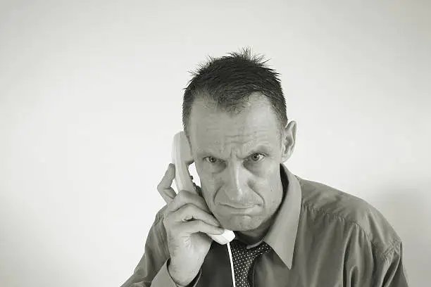 man in bsuiness shirt and tie looks very unhappy about the news on the telephone