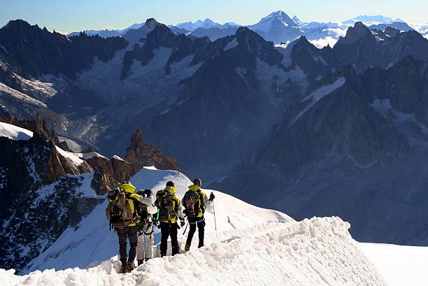 Alpine Climbers on Ridge at Mont Blanc, Chamonix, France DSLR picture of four Alpine climbers going down the ridge at l'Aiguille du Midi to reach the Mont Blanc summit. The climbers are on the foreground and the alps are in the background and the sky is clear. aiguille de midi photos stock pictures, royalty-free photos & images