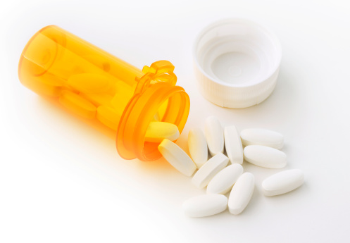 A still life of an open pill bottle of prescription medication with its contents poured out on a white background.