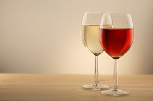 A warm toned image of a full wine glass of red wine  in front of a glass of white wine. Both glasses are resting on a plain wooden table against a plain background. Shot with shallow depth of field with focus on the foreground. With copyspace. 