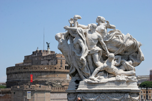 View of a statue cluster on a bridge on the Tiber River in Rome with the Castel Sant' Angelo in the background.