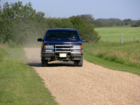 Navy blue truck driving down a gravel country road with dust being kicked up behind it
