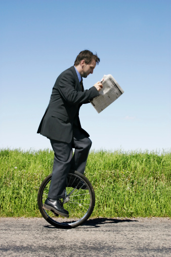 Businessman riding an unicycle and reading newspaper. Note that few parts are in motion.