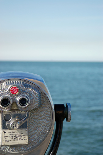 An old fashioned coin operated binoculars/telescope sits ready for use to observe the ocean.  The cost a mere quarter.