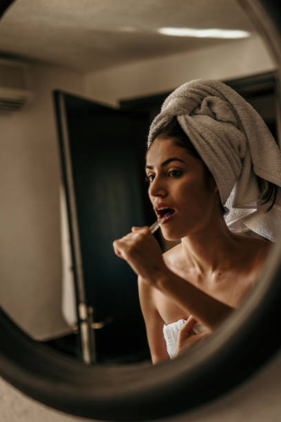 Latin beauty embraces her morning routine, wrapped in a towel and brushing her teeth in front of the bathroom mirror, radiating confidence and self-assuredness.