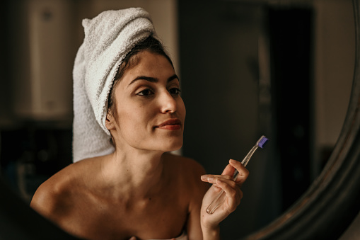 A Smiling pretty woman applying cream on her face in the bathroom.