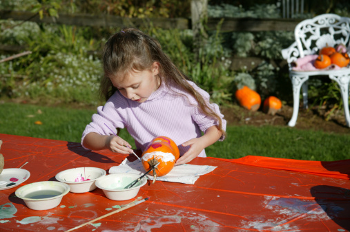 Little girl painting a pumpkin at a farm harvest festival