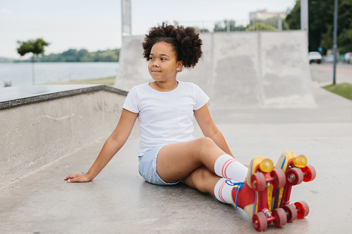 Cute little  girl roller skater sitting in city park and smiling.