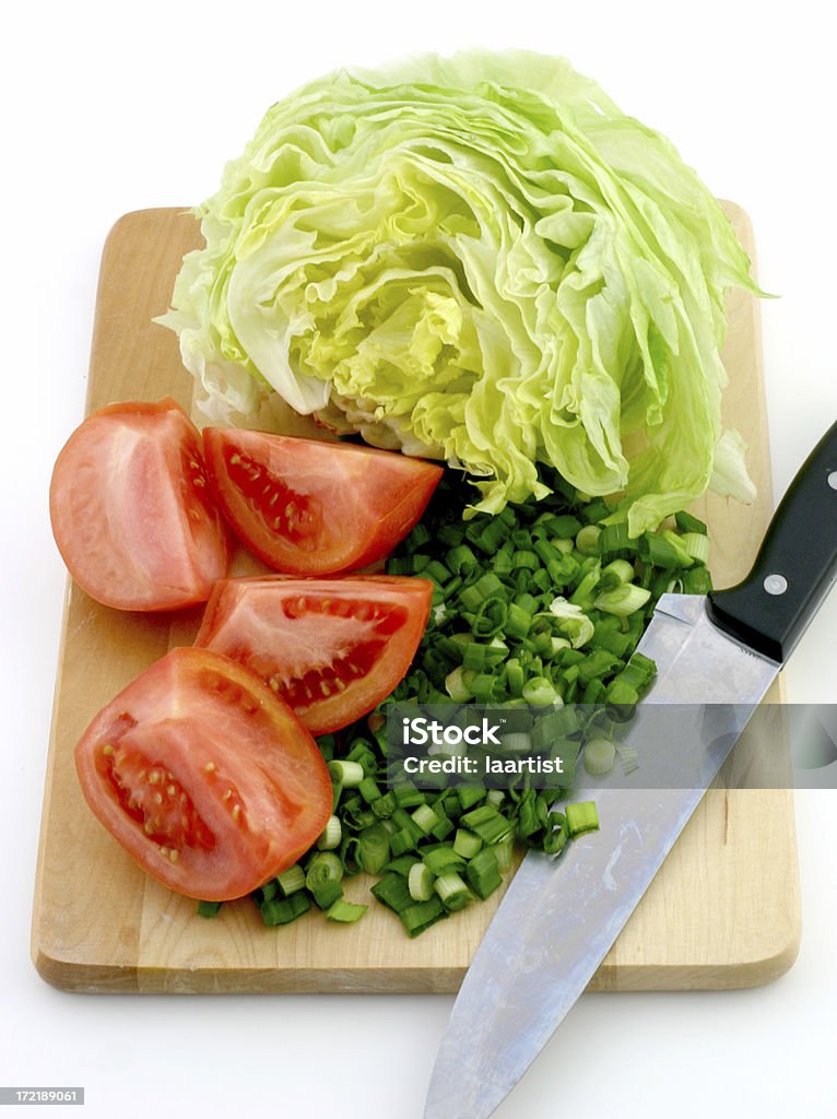 Chopping board. "A sliced tomato, chopped green onions and lettuce on a wooden chopping board with a knife." Cross Section Stock Photo