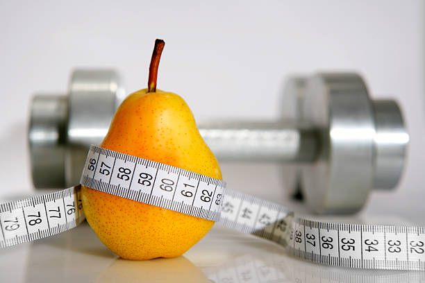 Close-up of a pear with a measuring tape around it and chrome dumbbells at the background. High resolution - 16 Mpx.