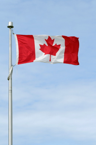 Canadian flag on a pole against a blue sky.