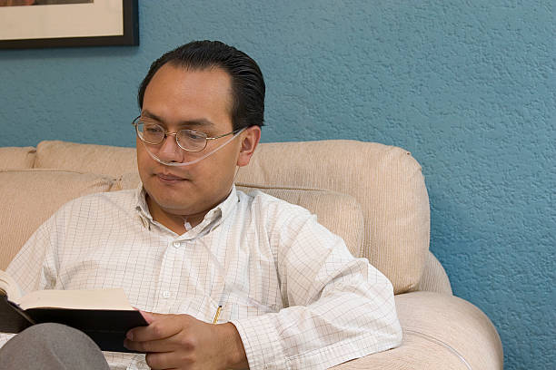 oxygen user oxygen user reading a book in his living room tracheotomy tubing stock pictures, royalty-free photos & images