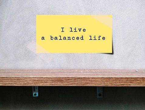 Note stick on wall over a shelf with text written I LIVE A BALANCED LIFE, positive mantra affirmation to remind oneself that living well-balanced life is crucial for healthy, happy and well-being life
