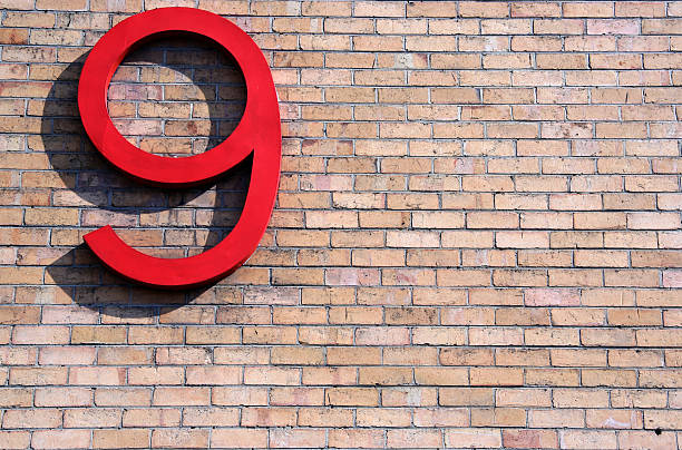 Red number nine with shadow on brick background