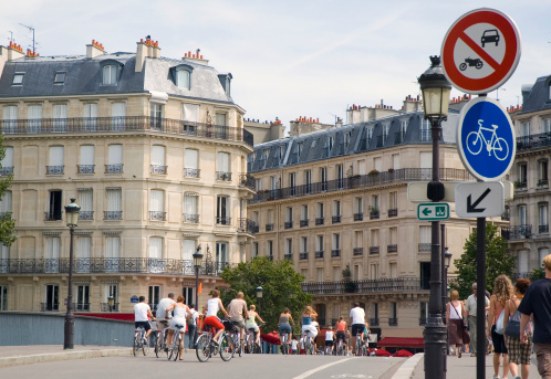 Group of bicycle riders crossing a bridge.  Street signs indicate they are entering an area where no motorized vehicles are allowed.Also see: