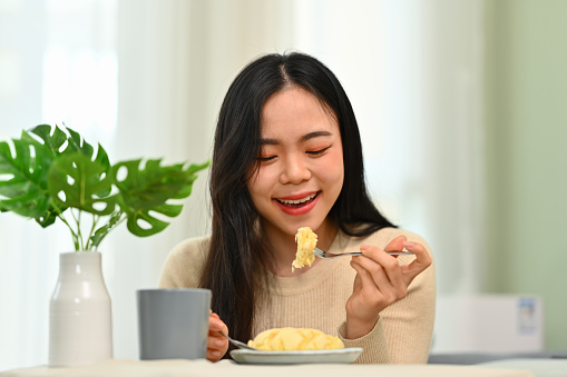 Happy young asian woman in casual clothes having breakfast at home. Concept of wellness, food and domestic lifestyle.