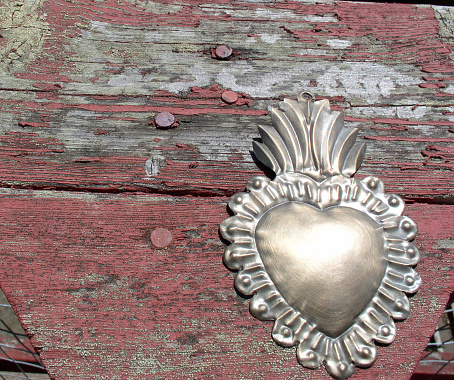 Sacred heart milagro on a peeling wood background.
