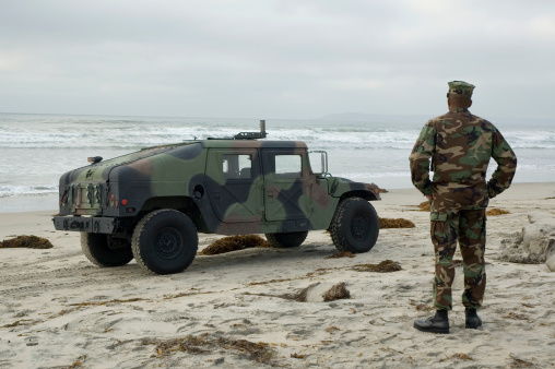 Military vehicle on the coastline with military officer standing by.